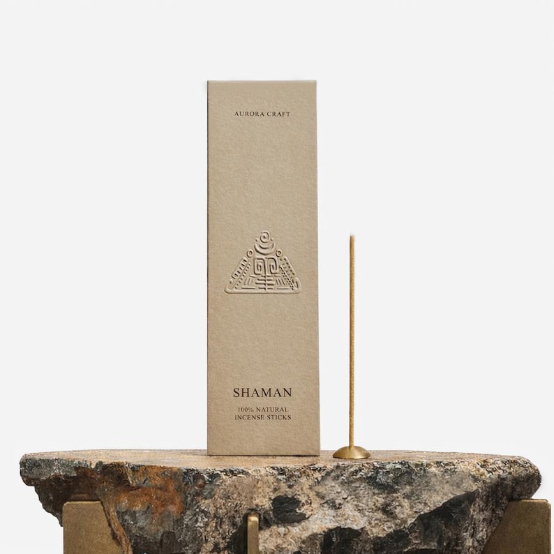 May include: A beige box of "SHAMAN" 100% natural incense sticks with a gold incense stick and holder. The box has embossed geometric designs and the text "AURORA CRAFT". The incense stick is standing on a stone surface.