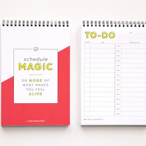 May include: A red and white spiral bound notebook with the text "schedule magic do more of what makes you feel alive" on the front cover. The back cover has a to-do list with a yellow header.