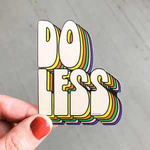 May include: A colourful sticker with the text "DO LESS" in a retro, layered font style. The letters are outlined in yellow, orange, green, blue and pink.