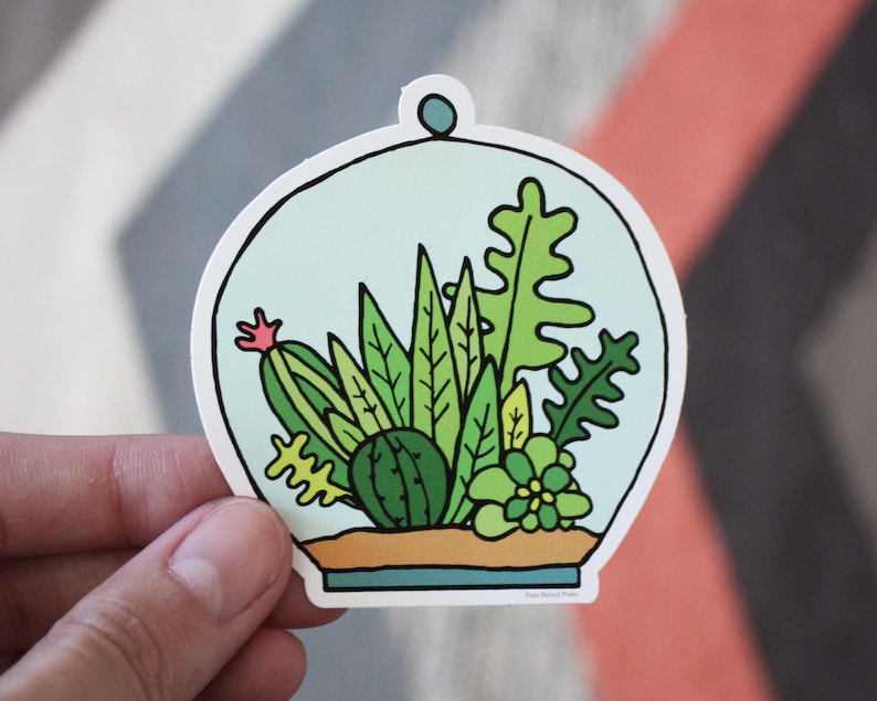 May include: A sticker of a glass dome terrarium with a variety of green plants and cacti inside. The dome is white with a blue top and the plants are drawn in a cartoon style.