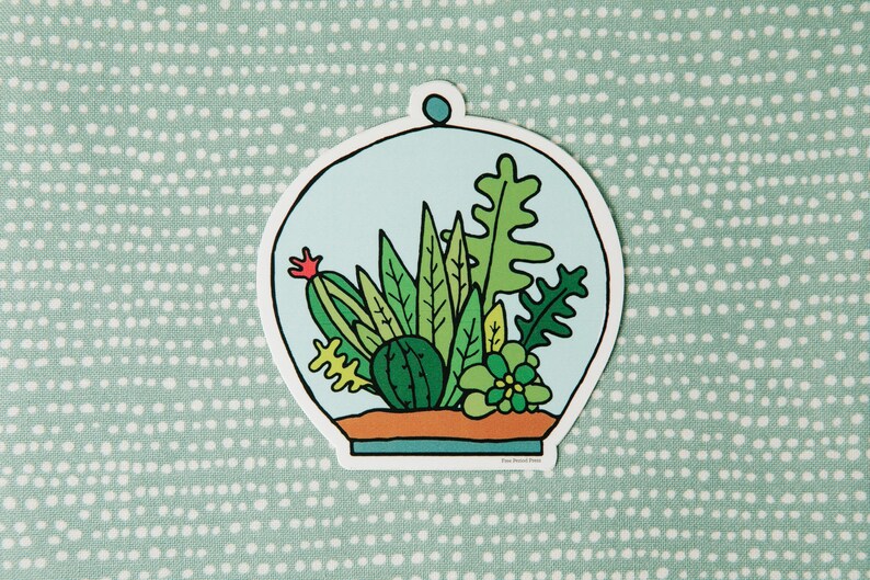 May include: A sticker of a glass terrarium with a variety of green plants, including a cactus, succulents, and ferns. The terrarium is on a light blue background with a white border.