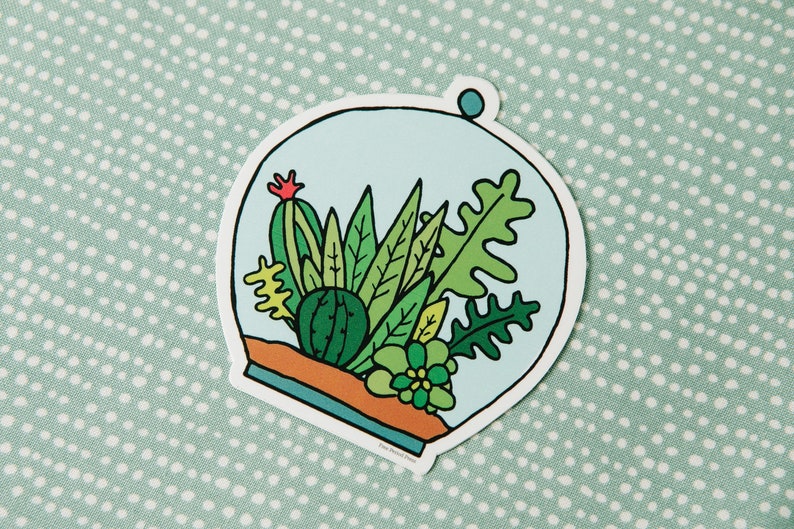 May include: A sticker of a glass dome with a variety of green plants inside. The plants are drawn in a cartoon style and include a cactus, succulents, and ferns. The dome is outlined in black and has a blue background.