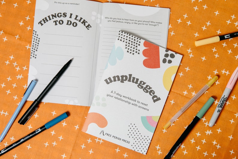 K&ouml;nnte beinhalten: Ein offenes Notizbuch mit den Worten "Things I Like To Do" auf dem Einband. Das Notizbuch liegt auf einer leuchtend orangenen Oberfl&auml;che mit wei&szlig;en Pluszeichen. Es gibt ein kleineres Notizbuch mit dem Titel "unplugged" und dem Text "A 7-day workbook to reset your relationship with screens" auf dem Einband. Das kleinere Notizbuch ist ge&ouml;ffnet und hat bunte abstrakte Formen auf dem Einband. Auf der Oberfl&auml;che liegen mehrere Stifte und Marker.