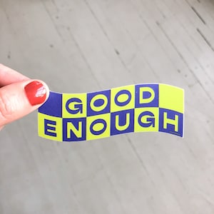May include: A yellow and purple sticker with the text "GOOD ENOUGH" in a checkered pattern.