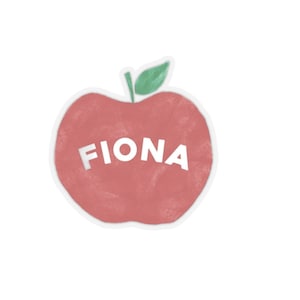 May include: A red apple-shaped sticker with the name "FIONA" cut out in white letters. The apple has a white outline and a green leaf at the top. The background is white.