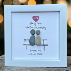 May include: A framed artwork celebrating a 40th wedding anniversary. The white frame surrounds a picture with the text "Happy Ruby Wedding Anniversary." Two pebble figures sit on a bench. The names "David & Sarah" and the date "September 27, 2020" are also included.