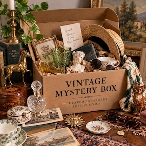 May include: A cardboard box labelled VINTAGE MYSTERY BOX containing assorted items including a green glass goblet, a straw hat, a small white bust, a floral teacup, a gold-tone sun ornament, a crystal perfume bottle, and a brass horse figurine.
