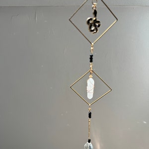 May include: A gold-toned crystal suncatcher with a clear crystal teardrop, a white crystal, and a black metal snake charm hanging from a gold-toned chain.