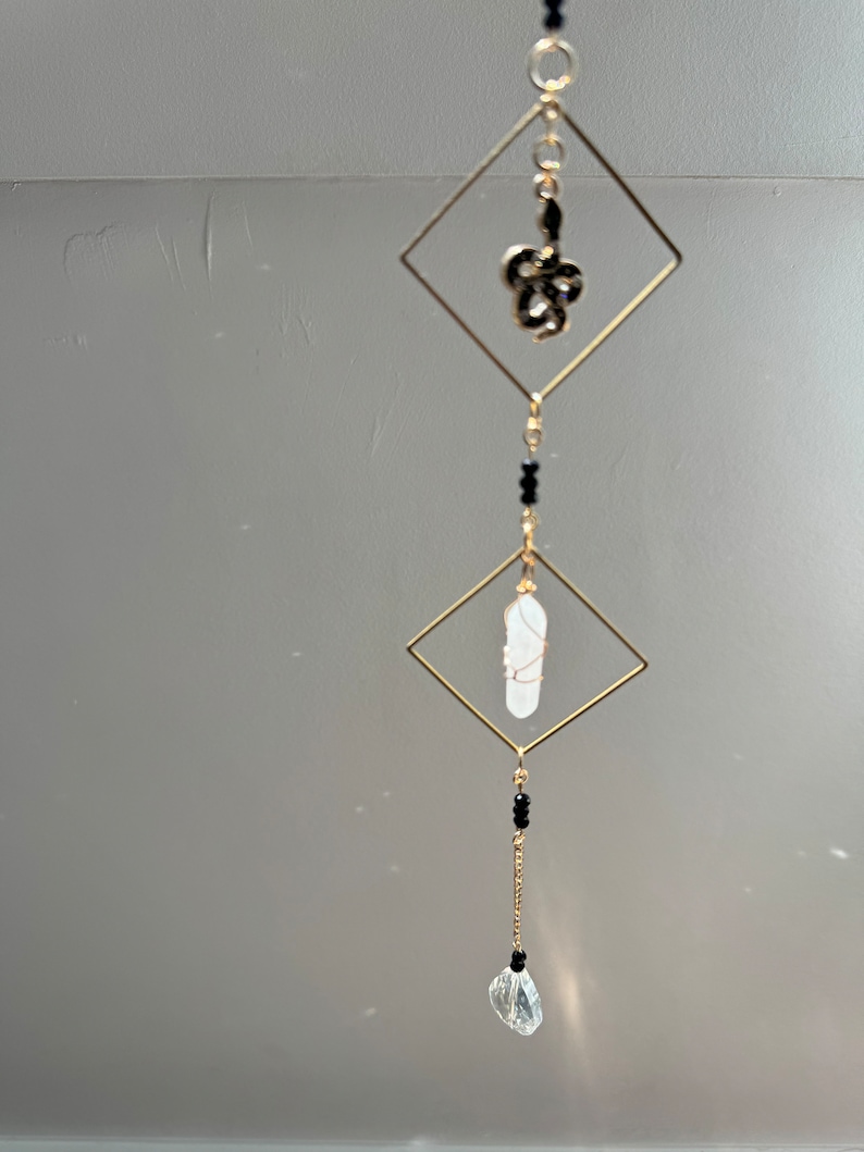 May include: A gold-toned crystal suncatcher with a clear crystal teardrop, a white crystal, and a black metal snake charm hanging from a gold-toned chain.