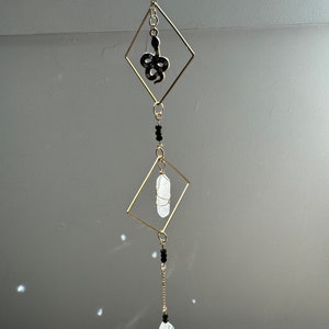 May include: A gold-toned crystal and snake charm hanging mobile. The mobile features a clear crystal, a black snake charm, and black beads.