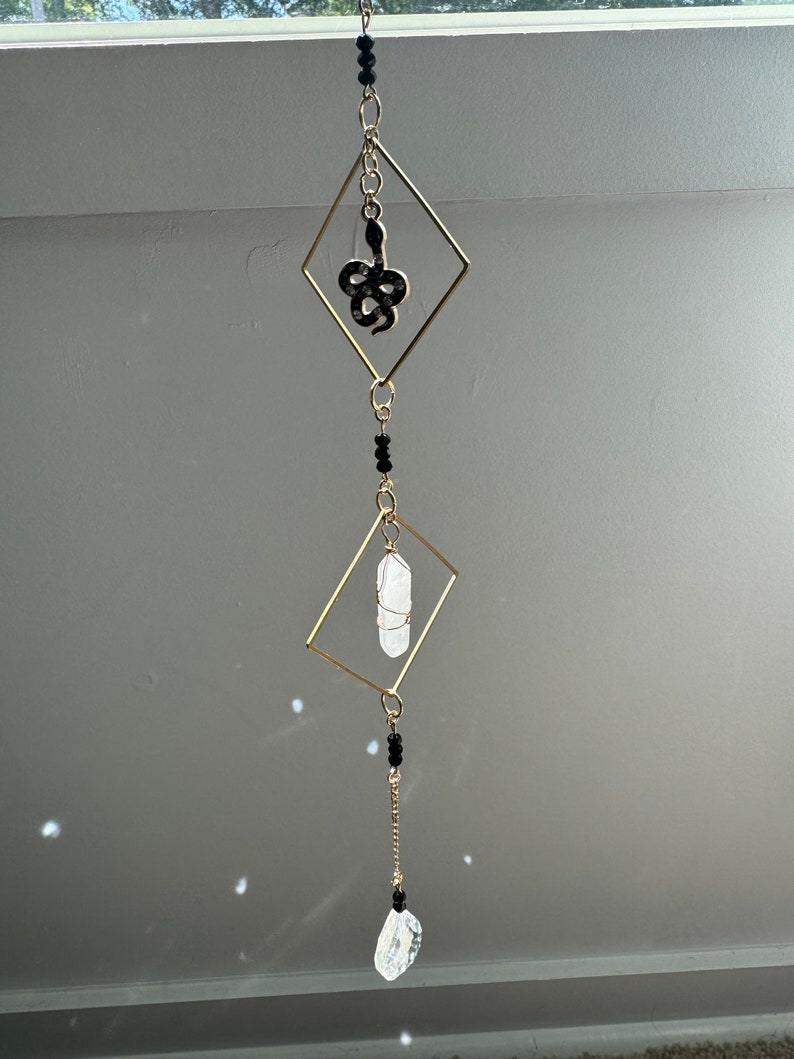 May include: A gold-toned crystal and snake charm hanging mobile. The mobile features a clear crystal, a black snake charm, and black beads.
