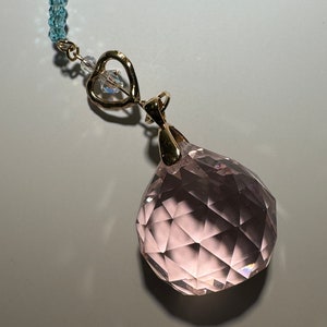 May include: A pink crystal ball pendant with a gold heart charm and a blue crystal bead necklace.