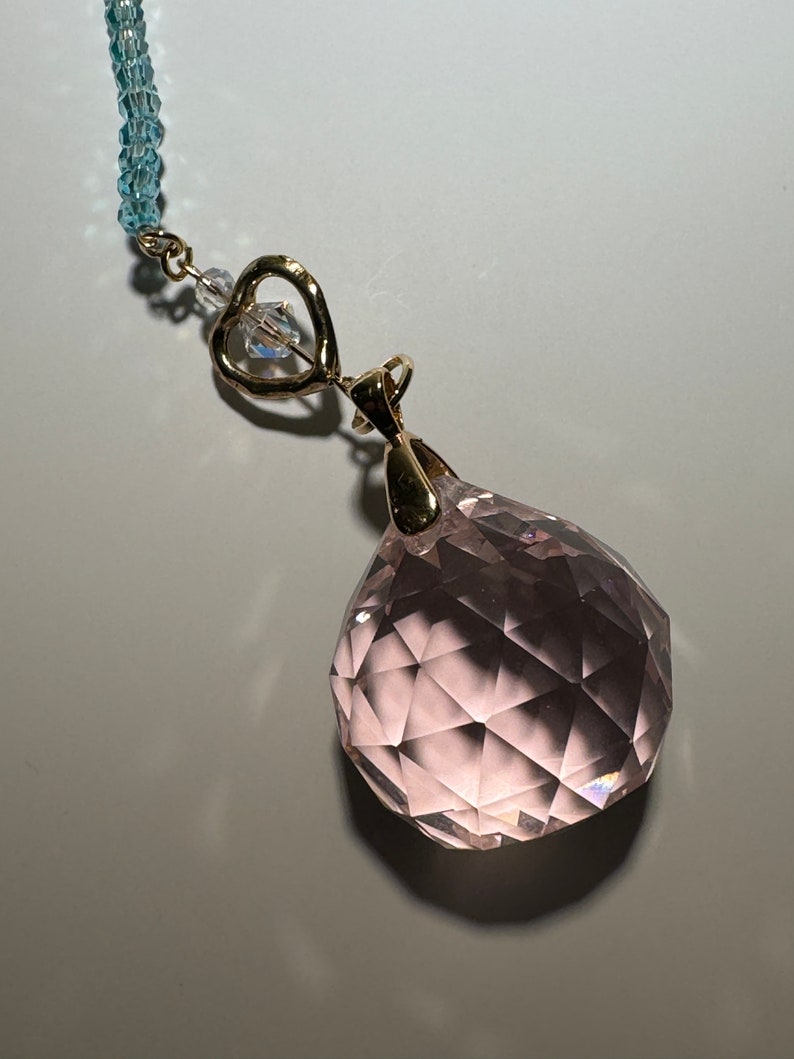 May include: A pink crystal ball pendant with a gold heart charm and a blue crystal bead necklace.