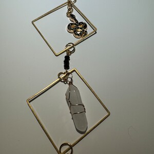 May include: A gold necklace with a white crystal pendant, a gold snake charm, and black beads.