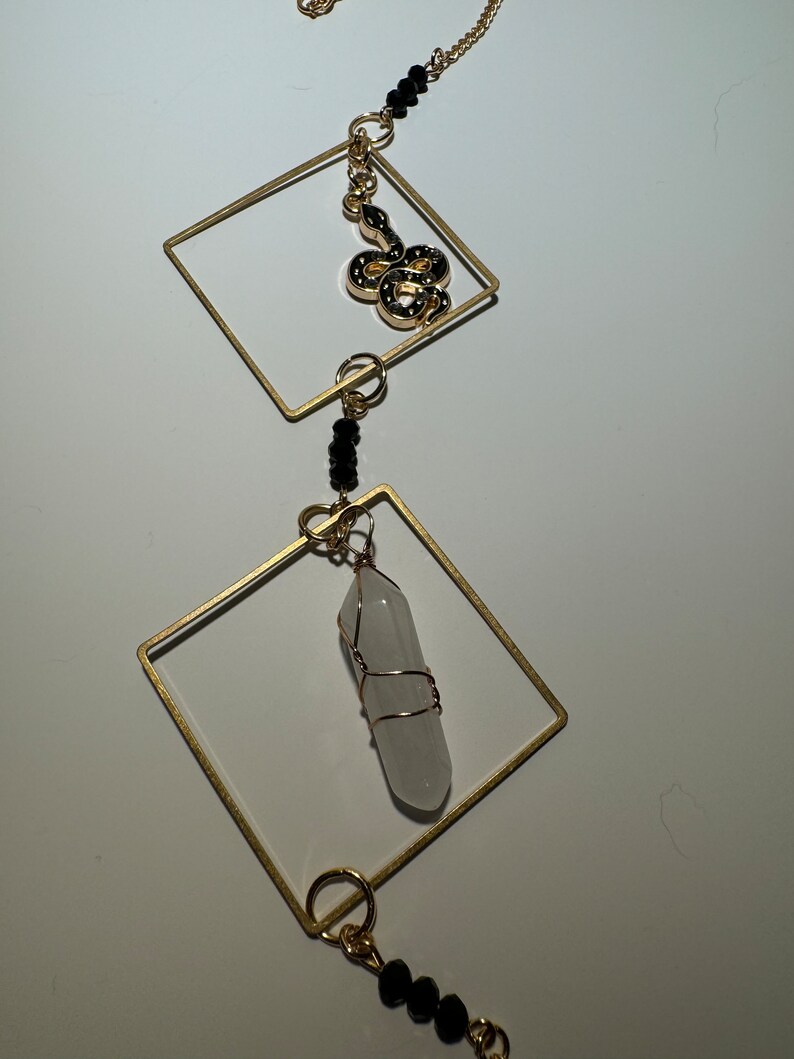 May include: A gold necklace with a white crystal pendant, a gold snake charm, and black beads.