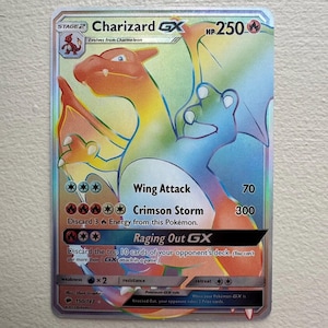 Puede incluir: Una carta de comercio de Pokemon holográfica con Charizard GX, un Pokemon de tipo fuego con colores naranja, amarillo y azul. La carta tiene 250 PS y presenta ataques como Ataque Ala, Tormenta Carmesí y Furia Desatada GX. La carta es de la serie Sol y Luna y tiene el número 150/147.