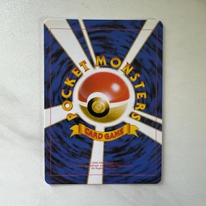 Puede incluir: Parte posterior de una carta de comercio de Pokemon con un fondo azul y un logotipo de Pokeball amarillo y rojo. El texto "Pocket Monsters Card Game" est&aacute; impreso en una pancarta amarilla.