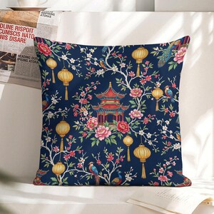 May include: Square decorative pillow with a dark blue background featuring a floral and pagoda design. The pattern includes pink flowers, yellow lanterns, and colorful birds. The pillow has a soft, inviting appearance.