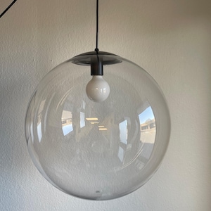 May include: A clear glass globe pendant light with a black metal fixture and a white bulb. The spherical shade reflects the surrounding environment. The light hangs from a black cord, offering a modern, minimalist design.
