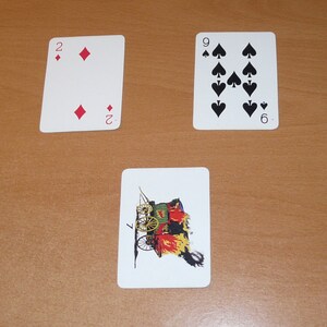 May include: Three playing cards on a wooden surface. The cards are a two of diamonds, a nine of spades, and a playing card with a picture of a wagon on fire.