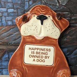 May include: Brown ceramic dog-shaped dish with a white plaque that reads "Happiness is being owned by a dog".
