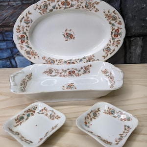 May include: A set of antique white porcelain serving dishes with floral patterns in orange, blue, and brown. The set includes an oval platter, a rectangular dish, and two small square dishes.