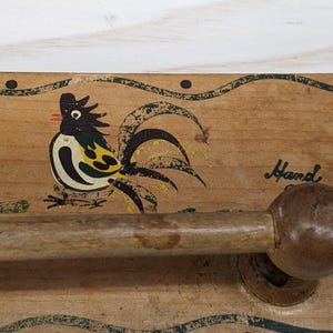 May include: Wooden wall-mounted towel rack with a hand-painted rooster design. The rack has a wooden knob and the words "Hand" are painted on the wood.