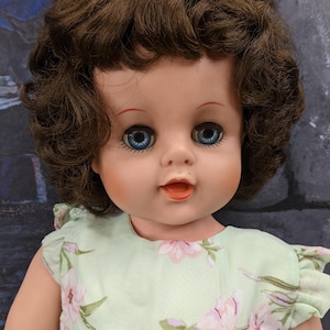 May include: A vintage doll with brown curly hair, blue eyes, and a light green dress with a floral pattern.