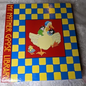 May include: A children's book titled "My Mother Goose Library." The cover shows a large yellow goose wearing a blue hat, carrying three small animals. The background has a red centre and a blue and yellow checkerboard pattern.