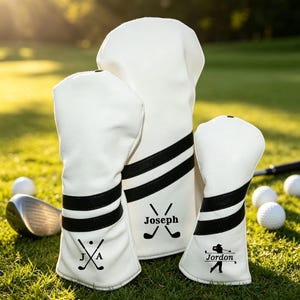 May include: A set of three white golf club head covers featuring two black horizontal stripes. Each cover is personalized with black text and graphics: the letters J and A with crossed clubs, the name Joseph with crossed clubs, and the name Jordon.