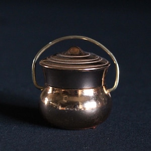 May include: A small, copper-colored pot with a lid and a gold-colored handle. The pot has a hammered finish and a rounded shape.