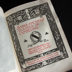 Pode incluir: Uma capa de livro vintage com uma ilustração em preto e branco de uma coroa e um escudo. O título do livro é "Shakespeare's Tragedy of Cymbeline" com um prefácio e um glossário por Israel Gollancz, M.A. O livro foi publicado por David McKay em 1922 na Filadélfia, PA.