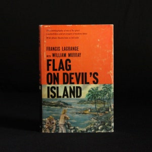 May include: A book cover with an orange background and black text that reads "Flag on Devil's Island". The text is in a bold, sans-serif font. The cover features an illustration of a tropical island with palm trees and a beach.