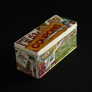 Puede incluir: Una caja de lata rectangular con un diseño colorido que presenta la palabra "COUPONS" en letras grandes. La caja está decorada con imágenes de tijeras, dinero y otros artículos relacionados con los cupones.