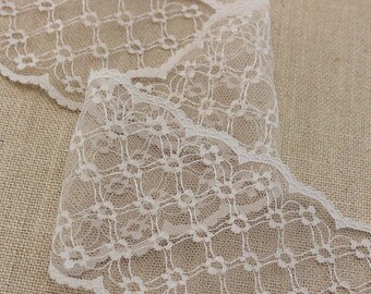 May include: White lace trim with a delicate floral pattern. The lace has a scalloped edge and is perfect for adding a touch of elegance to any project.