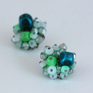 May include: A pair of green and blue beaded earrings. The earrings are made of small, round beads in shades of green and white, with a larger, square blue bead in the center of each earring.