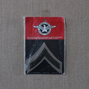 Puede incluir: Un paquete de dos insignias de rango militar, galones de sargento, en una bolsa de plástico. El paquete está etiquetado "Hilborn-Hamburger Military Insignia" e incluye el texto "This item is warranted by the manufacturer to meet the applicable Government requirements. USN Number H24N. USMC No. as stamped."