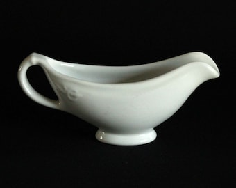 Puede incluir: Una salsera de porcelana blanca con asa. La salsera tiene una forma redonda y lisa y una base pequeña.