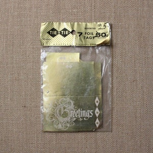 May include: A package of 7 gold foil gift tags with the words "Greetings" printed on them. The package is labeled "Tie-Tie" and "Assorted Foil Tags 25c 50c".