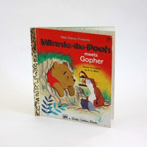 Könnte beinhalten: Ein Vintage-Buch aus der Little Golden Book-Reihe mit Winnie Puuh, einer beliebten Kinderfigur, die Gopher trifft. Das Cover zeigt Illustrationen von Winnie Puuh und Gopher in einer Waldlandschaft. Der Titel des Buches lautet "Winnie Puuh trifft Gopher" und basiert auf einer Geschichte von A. A. Milne.
