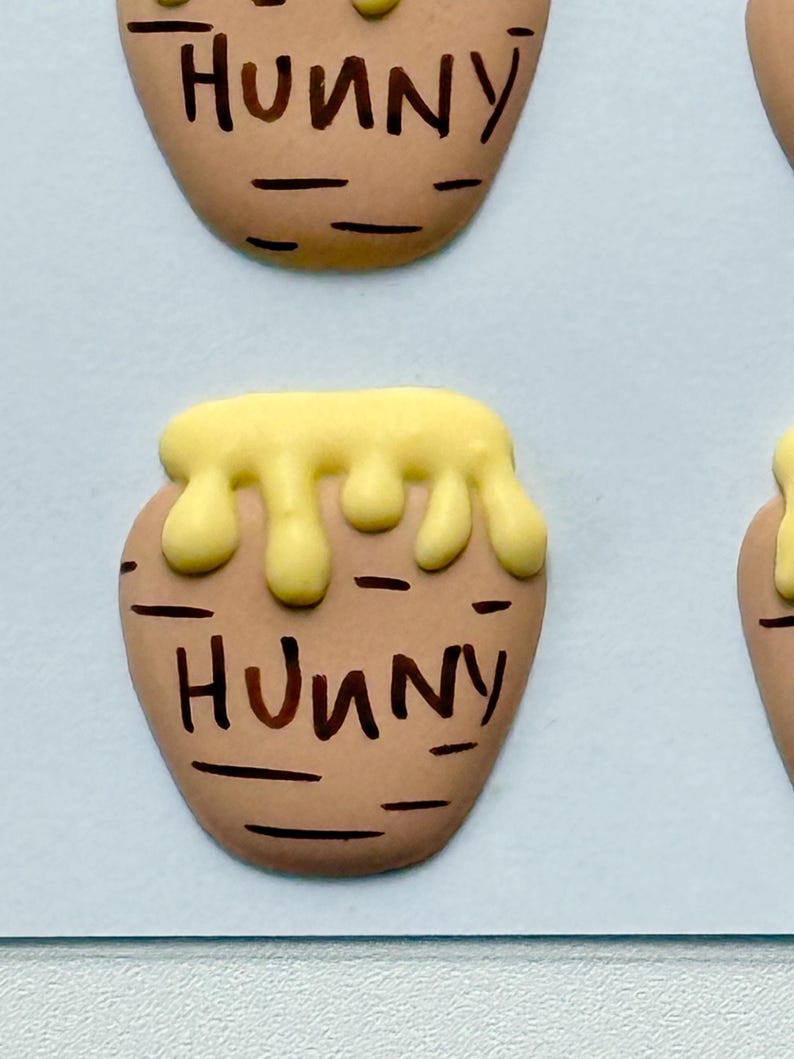 May include: Close-up of several brown, oval-shaped objects resembling honey pots. Each pot has a yellow, dripping honey design at the top and the word "Hunny" written in brown.