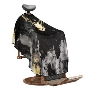 May include: Black barber's cape with a gold chain and a gold razor design. The cape is draped over a barber's chair.