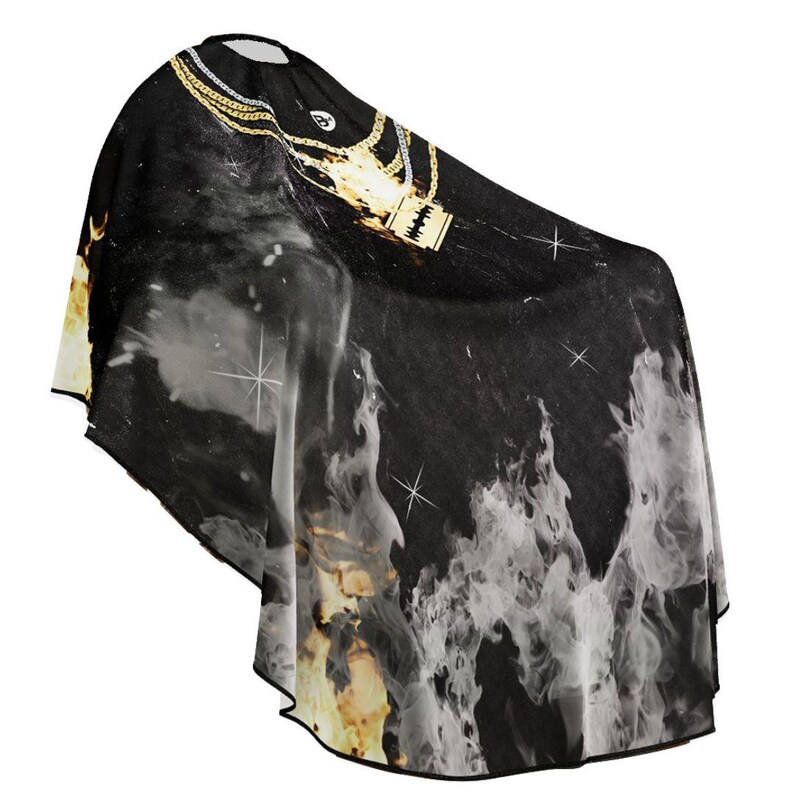 May include: Black barber cape with a gold chain and a gold pendant featuring a microphone design. The cape has a white and grey flame design.