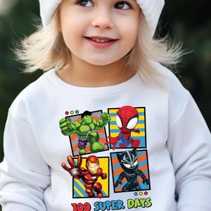 A young girl wearing a white beanie and a white sweater with a graphic of four cartoon characters: the Hulk, Spider-Man, Iron Man, and Black Widow.