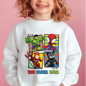 A young girl wearing a white sweatshirt with a graphic of four superhero characters: the Hulk, Spider-Man, Iron Man, and Black Widow, along with the text "100 Super Days".
