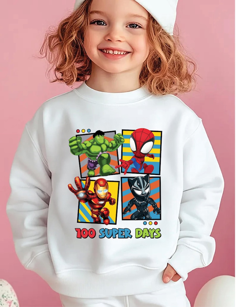 A young girl wearing a white sweatshirt with a graphic of four superhero characters: the Hulk, Spider-Man, Iron Man, and Black Widow, along with the text "100 Super Days".