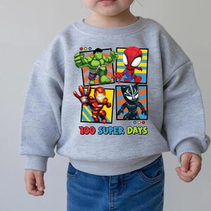 A child wearing a gray sweatshirt with a graphic of four superhero characters: Hulk, Spider-Man, Iron Man, and Black Widow, along with the text "100 SUPER DAYS".