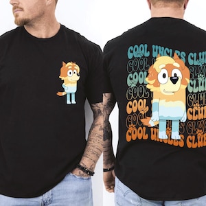 May include: Black t-shirt featuring a cartoon dog character with orange and blue coloring. The front of the shirt has a small image of the character. The back of the shirt has the text "COOL UNCLES CLUB" in a repeating pattern.