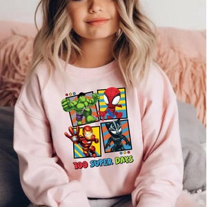A young girl wearing a pink sweatshirt with a graphic of four cartoon characters: the Hulk, Spider-Man, Iron Man, and a character with a face.