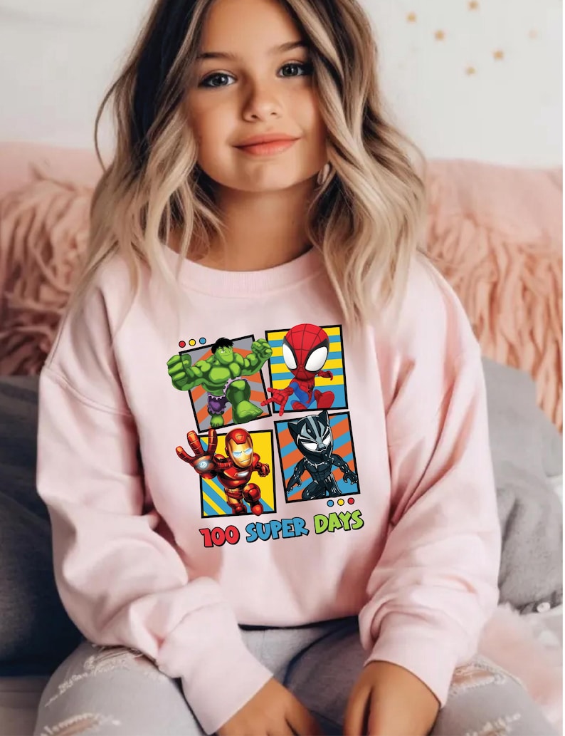 A young girl wearing a pink sweatshirt with a graphic of four cartoon characters: the Hulk, Spider-Man, Iron Man, and a character with a face.